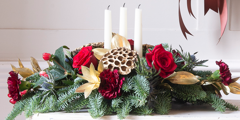 Christmas table centre with pine, carnations, roses, and candles. 