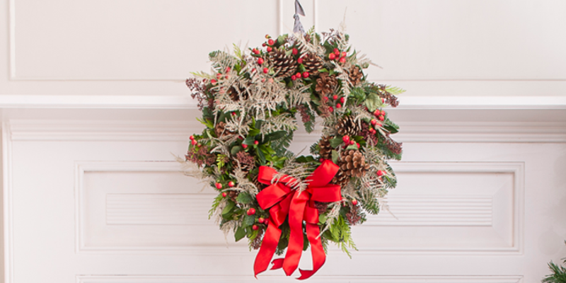 Christmas wreath with red ribbon hung on white wall. 