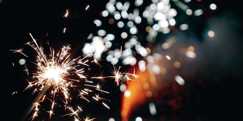 Dark night sky with a sparkler and firework sparks starkly contrasted against it, photo by Alexander Kagan