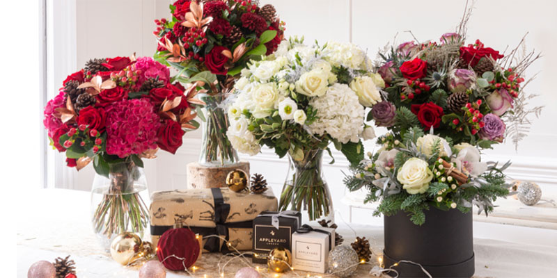 Five Christmas bouquets surrounded by chocolates, baubles, and presents.