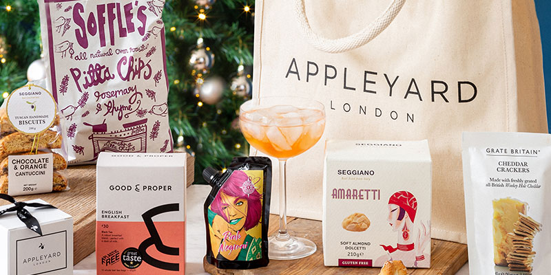 Christmas hamper on a table with Appleyard jute bag, pitta chips, biscuits, cocktail, tea & chocolates. 