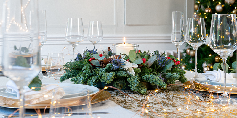 A Christmas table centre with a candle on a table with fairy lights, glasses, and plates. 