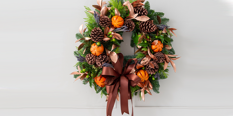 A spruce Christmas wreath with pinecones, dried oranges, copper leaves, and a bronze bow. 